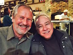 Two men in a restaurant huddle into the frame and smile at the camera.