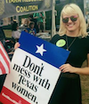 A woman in sunglasses smiles amiably and holds a sign that reads Don't Mess with Texas Women.
