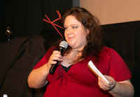 A woman holding index cards in one hand speaks into the microphone she is holding with the other.