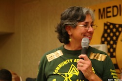 A woman holding a microphone to her mouth laughs at something off camera