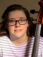 A young woman in glasses smiles placidly at the camera. The bow a cello is visible in front of her shoulder.