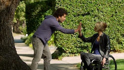 A man leans over to give a high five to a woman sitting in a wheelchair, who seems a bit bewildered.