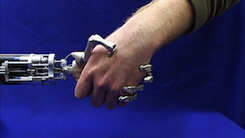 Against a deep blue background, a spindly robotic hand grips a human hand.