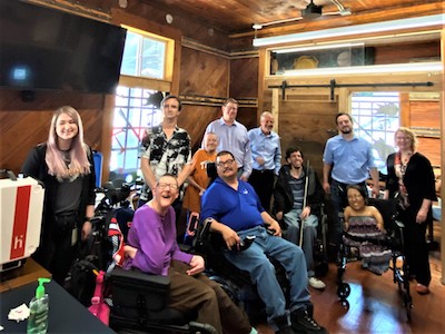 11 people, many with assistive devices and or visible disabilities, gather for a group photo.
