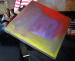 A painting with swaths of yellow, purple-blue, and red paint sits on one of its corners in a director's chair.