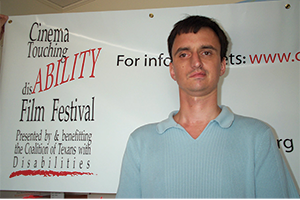 A man stands in front of a large red, black, and white Cinema Touching Disability Fim Festival banner.