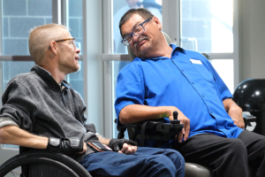 Two men in wheelchairs look at each other laughing