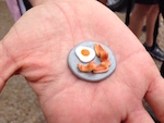 On an open palm sits a tiny ceramic figure of a plate of bacon and eggs.