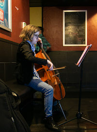 In profile, a young woman concentrates on sheet music on a stand as she plays the cello.