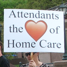 A woman holds a sign that reads Attendants the heart of Home Care