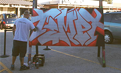 A man with his back to the camera spray paints the word 