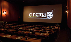 A dark movie theater shows the Cinema Touching Disability logo on its screen